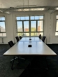 Leerer Konferenzraum mit Tisch, schwarzen Stühlen und Aussicht auf die Stadt durch große Fenster.