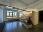 Ein leerer Seminarraum mit Holzbänken und Teppich, großen Fenstern, sieht modern und geräumig aus.