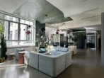 Großer, heller Raum mit modernen Möbeln; graue Sofas, farbige Lampen und Grünpflanzen.