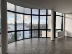 Leerer, heller Raum mit strukturiertem Boden und großen, gebogenen Fenstern mit Blick auf die Stadt.