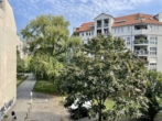 Städtische Szene mit Gebäuden, grünem Baum und blauem Himmel unter leichter Bewölkung.