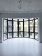 Ein großer, gebogener schwarzer Fensterrahmen mit Blick auf gelbe Außenfassaden.