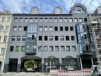 Ein modernes, mehrstöckiges graues Gebäude mit großen Fenstern und markanten runden Dachfenstern.