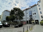 Mehrstöckiges Wohngebäude in grauer Farbe, bedeckt von Bäumen und einem gesprenkelten Himmel.