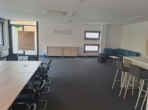 Besprechungsraum mit grauem Teppich, Holztisch, Stühlen, Lounge-Bereich und Logo an der Wand.